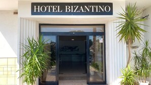 The entrance to Hotel Bizantino with a clear sign above the door, potted plants on either side, and a tiled patio area. - Hotel Bizantino (Massafra)