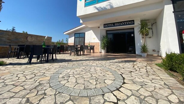 A modern hotel with a stone-paved courtyard, outdoor seating, and a clear blue sky. - Hotel Bizantino (Massafra)