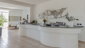 A reception area with a curved white counter, a wall-mounted painting, and a potted plant. - Hotel Bizantino (Massafra)