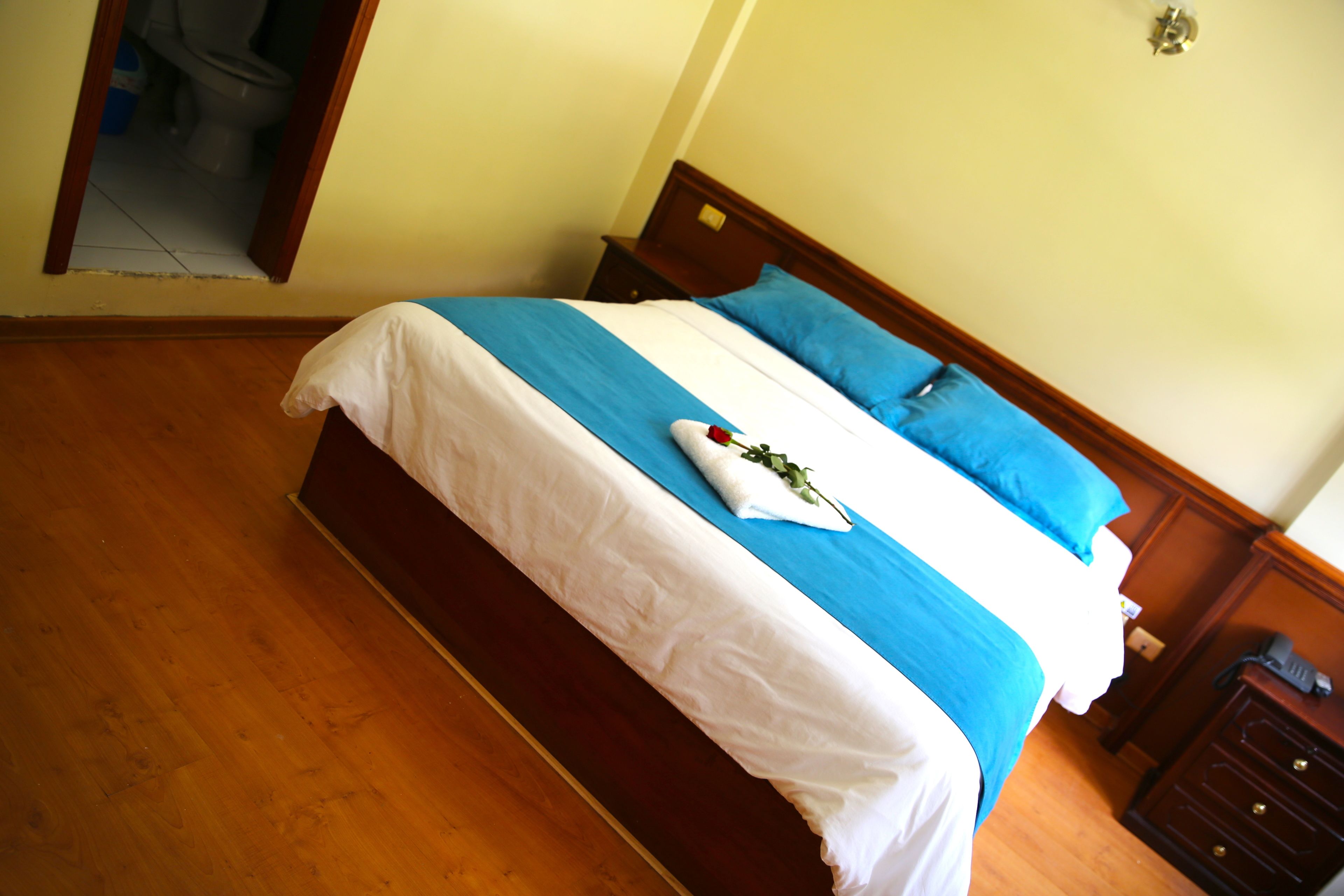 A neatly made bed with a blue and white bedspread, a white pillow, and a decorative rose.
