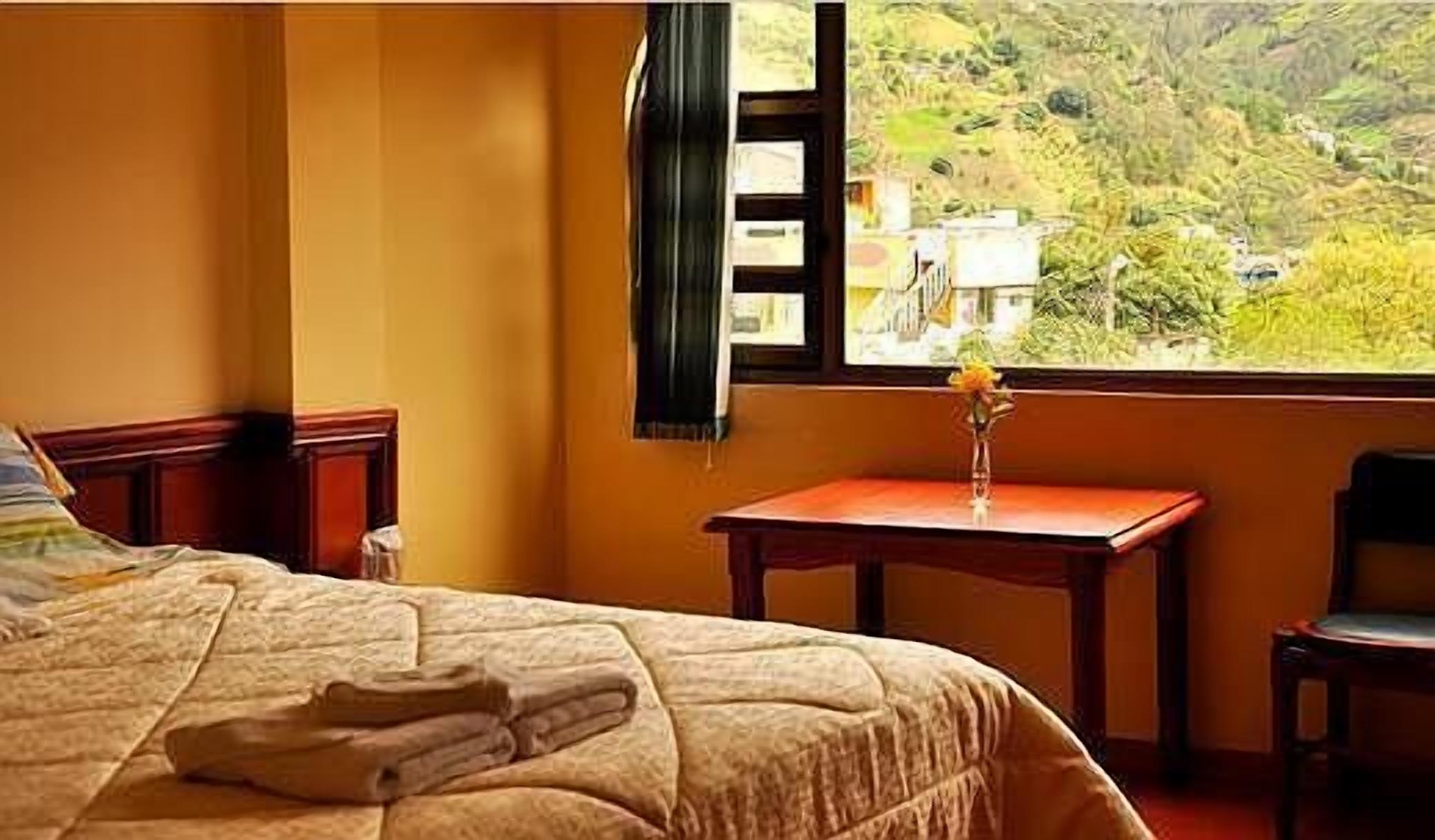 A hotel room with a bed, a small table with a vase, and a view of a mountainous landscape.