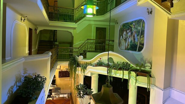 Un interior de varios niveles con una imponente escalera, barandillas ornamentales y plantas colgantes.