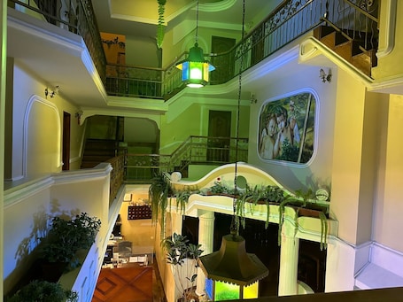 A multi-level interior with a grand staircase, ornate railings, and hanging plants.