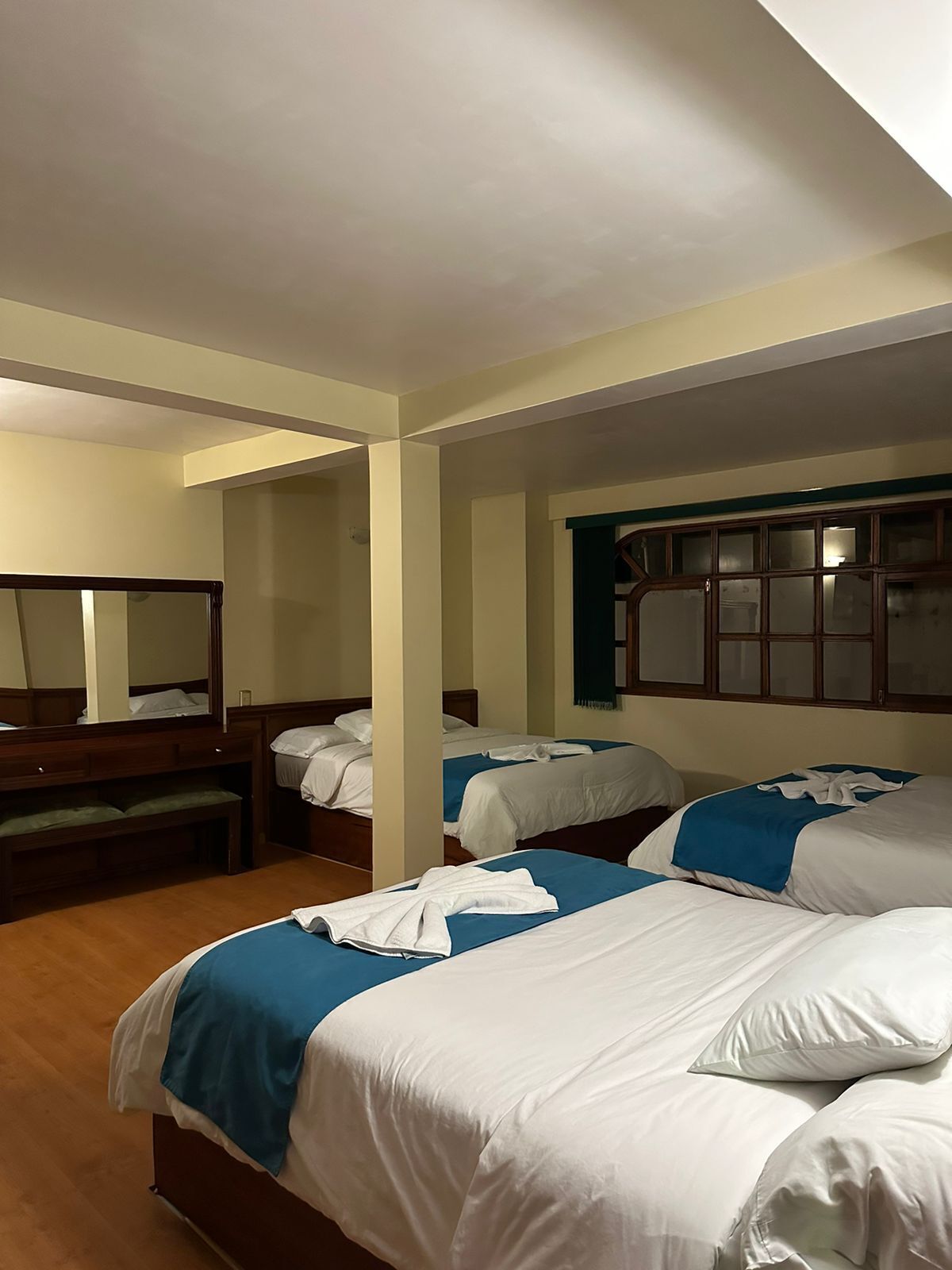 A hotel room with three beds, wooden headboards, and a large mirror on one wall.