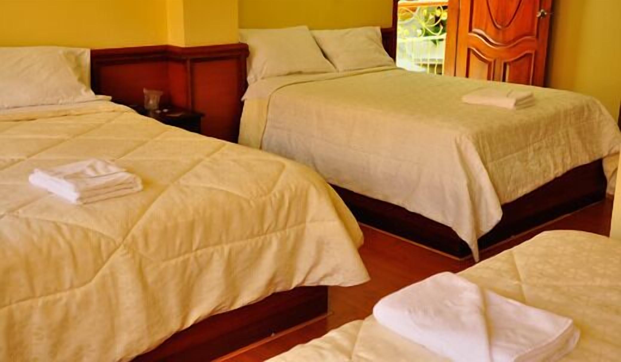 Habitación de hotel con dos camas, cada una con una toalla blanca doblada con cuidado.