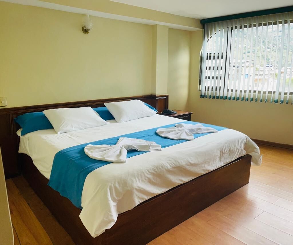 Una cama bien tendida con ropa de cama blanca y azul, un cabecero de madera y una mesita de noche con un teléfono.