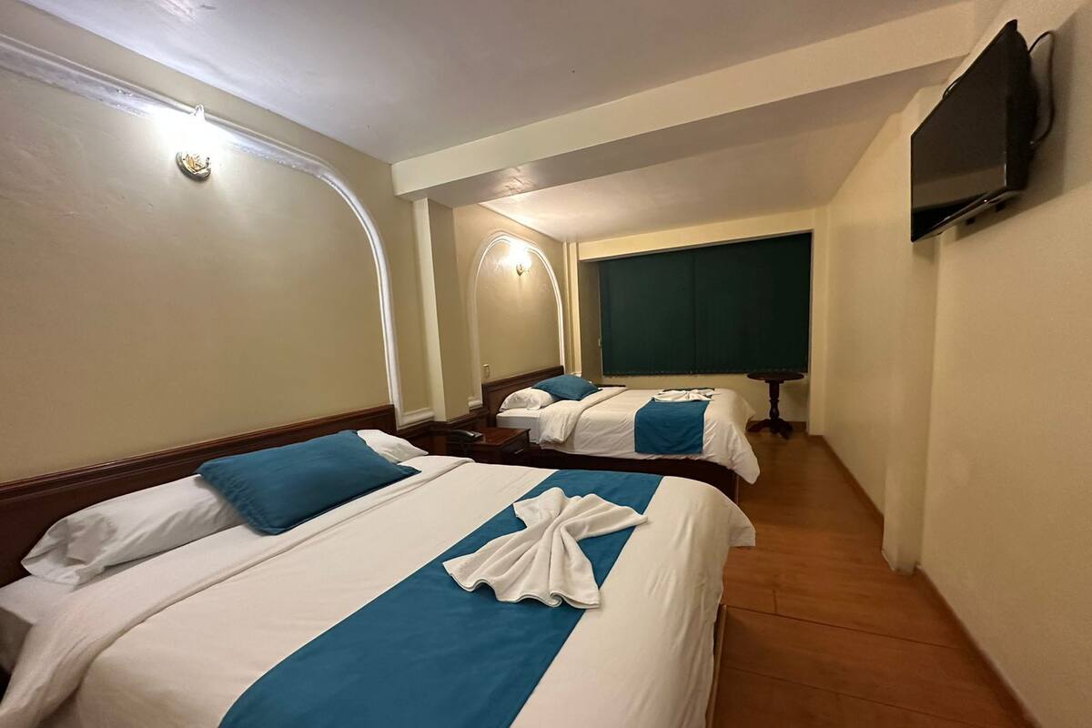 Een hotelkamer met twee bedden, elk voorzien van blauw-witte beddengoed, een wandgemonteerde flatscreen-tv en een houten vloer.