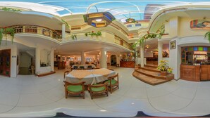 Un amplio atrium con techo alto, varios niveles y una zona de comedor central con mesas y sillas.