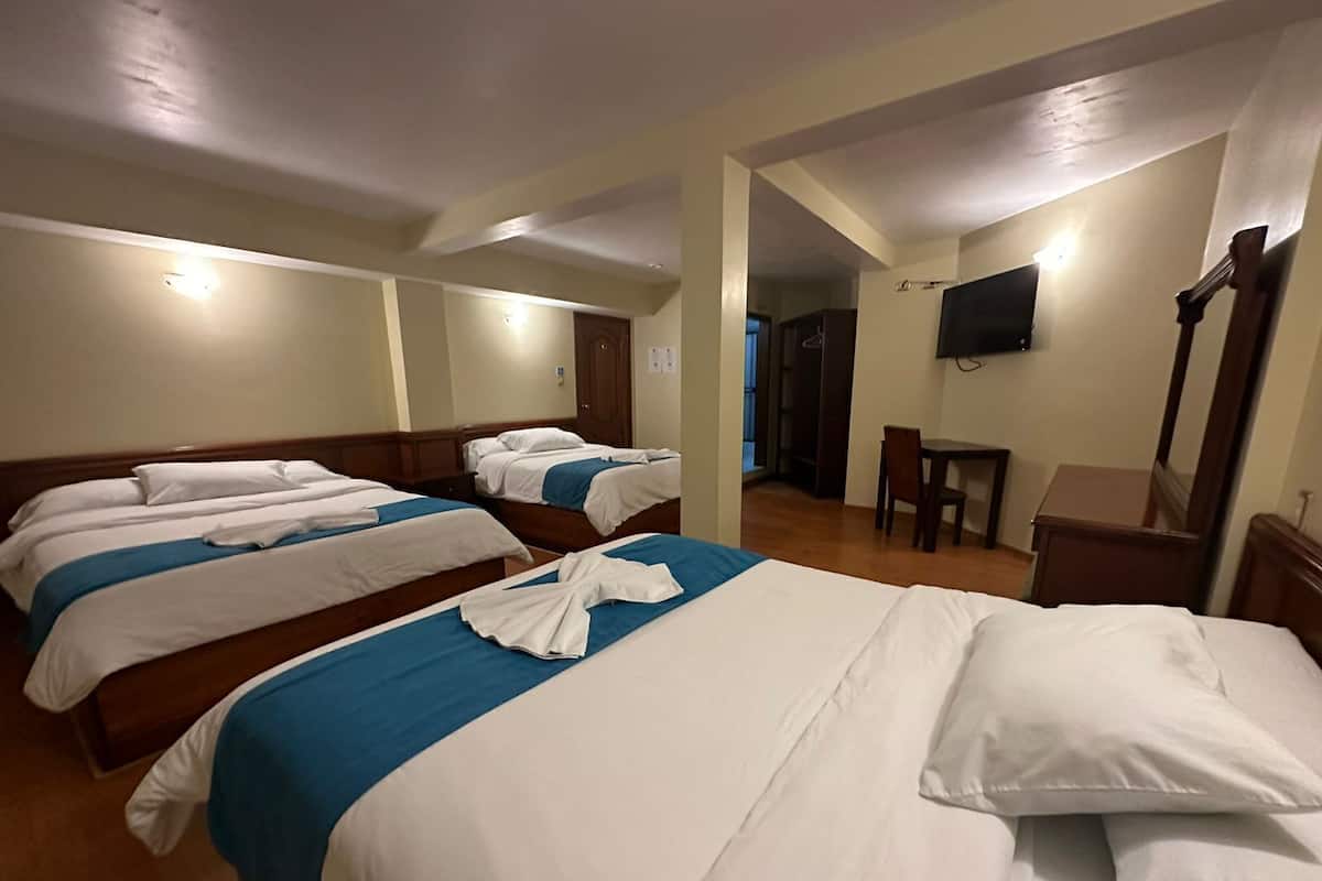 Een hotelkamer met drie bedden, een bureau en een televisie.