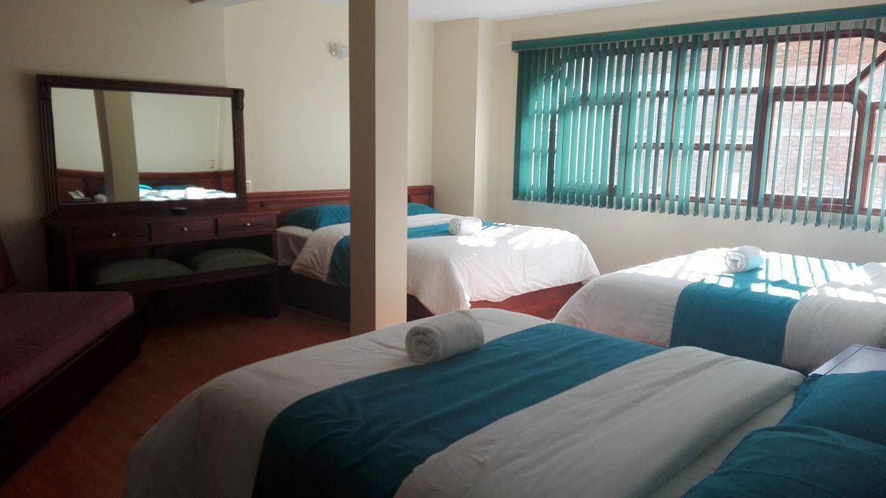 A hotel room with two beds, a wooden dresser, a large mirror, and a window with green blinds.