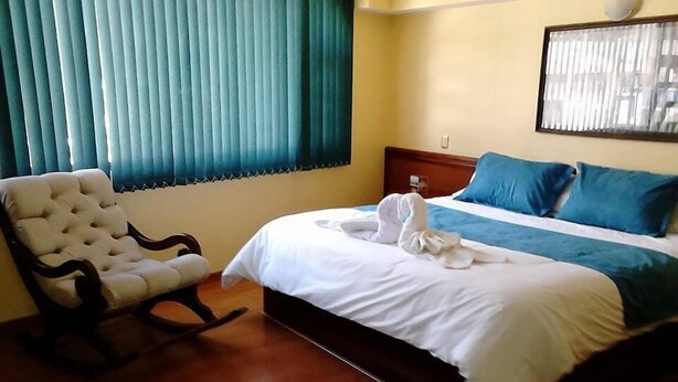 Une chambre d’hôtel avec un lit, une chaise et une fenêtre avec des stores.