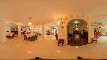 A spacious hotel lobby with multiple dining areas, a reception desk, and a Christmas tree.