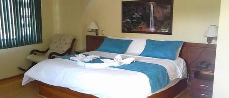 A neatly made bed with blue and white bedding, a chair, a nightstand with a lamp, and a painting of a waterfall on the wall.