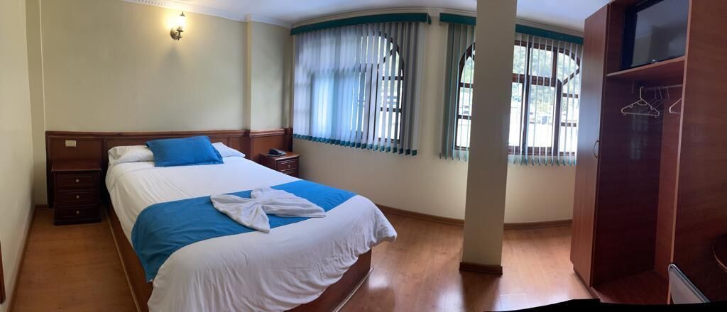 A hotel room with a bed, a nightstand, a wardrobe, and a window with curtains.