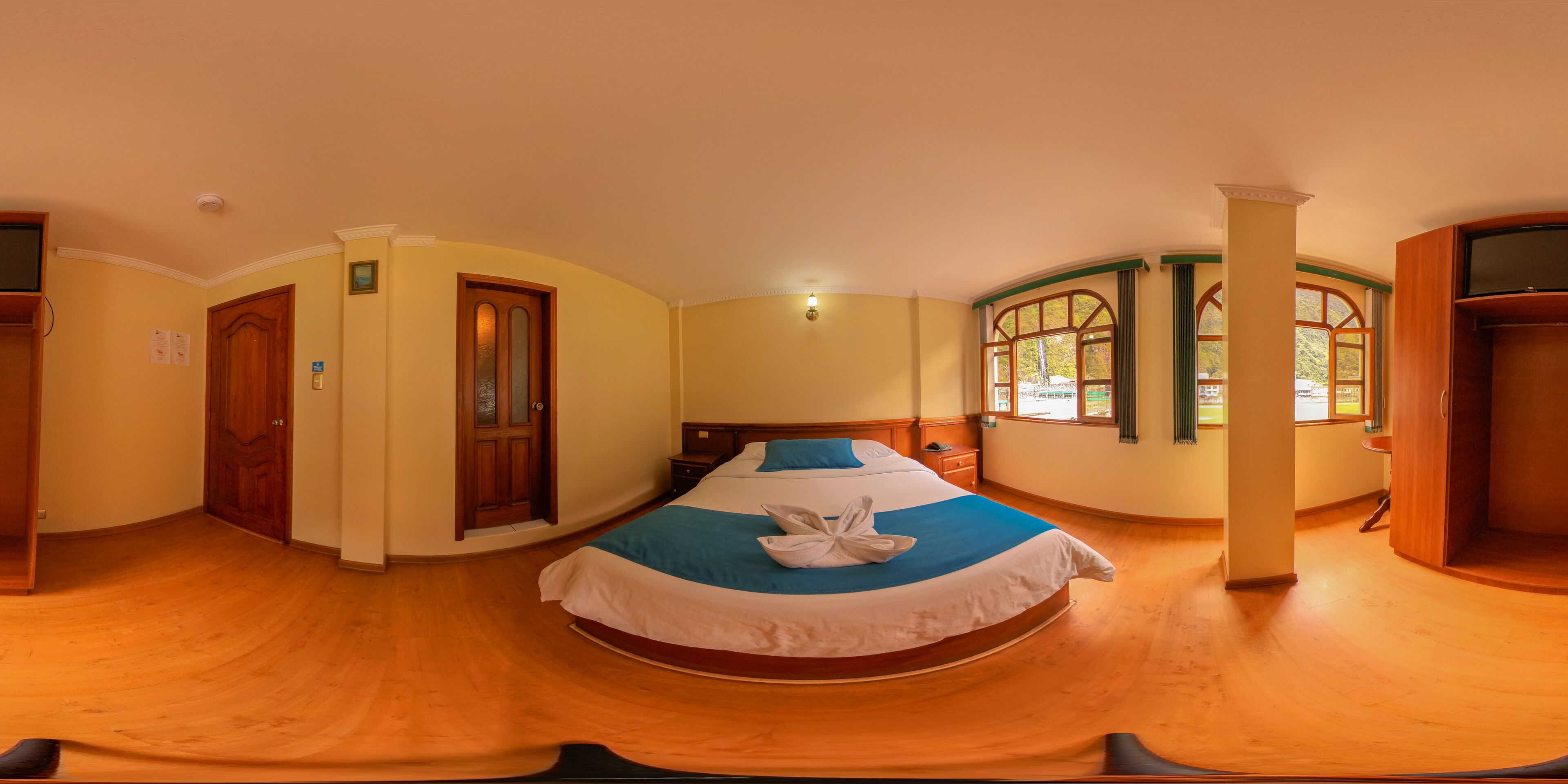 Una habitación circular con una cama en el centro, suelo de madera, una puerta y ventanas con vistas.
