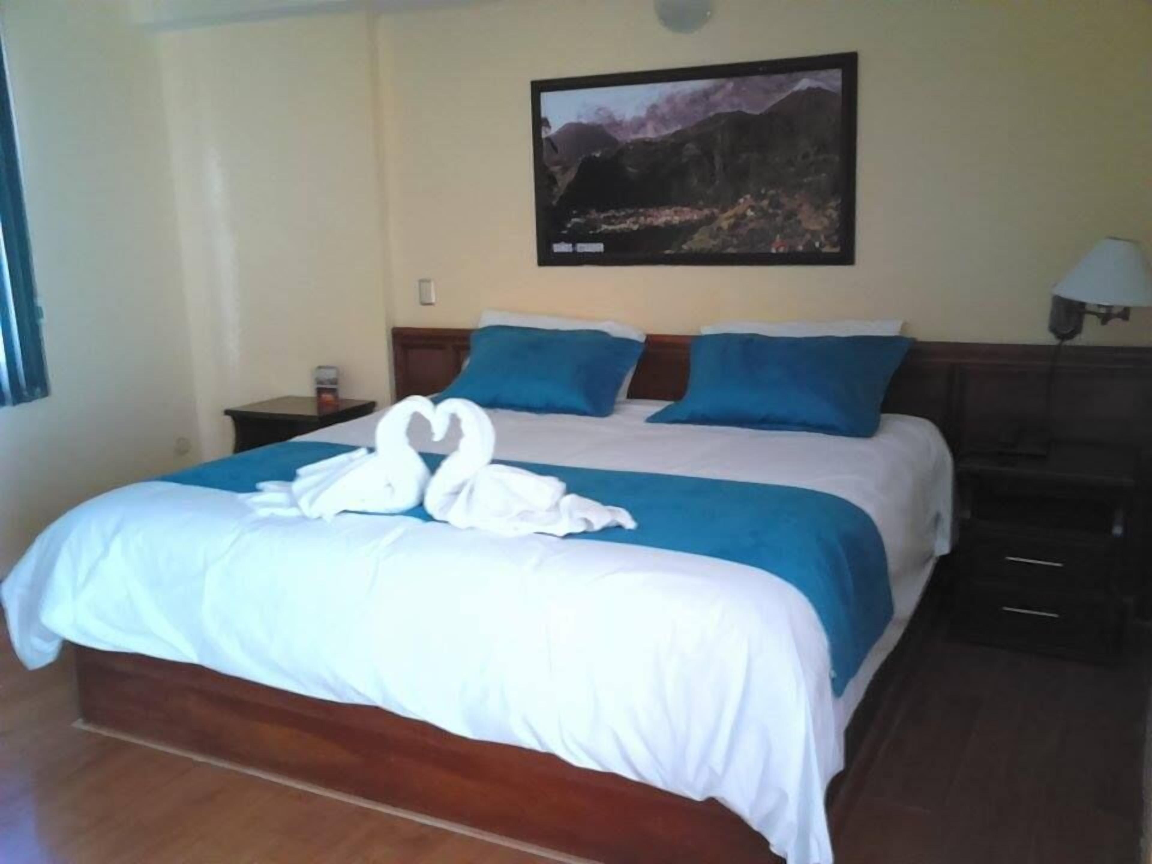 A hotel room with a large bed, blue and white bedding, a framed picture on the wall, and a wooden floor.