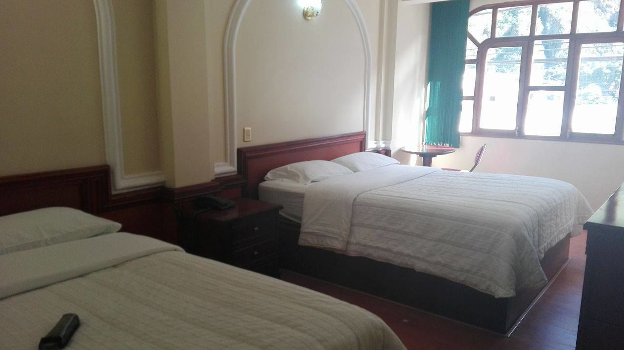 Una camera d'albergo con due letti, un comodino, una lampada e una finestra con tende.