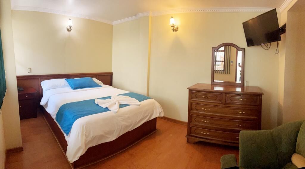 Una camera d'albergo con un letto, una cassettiera e un televisore montato a parete.