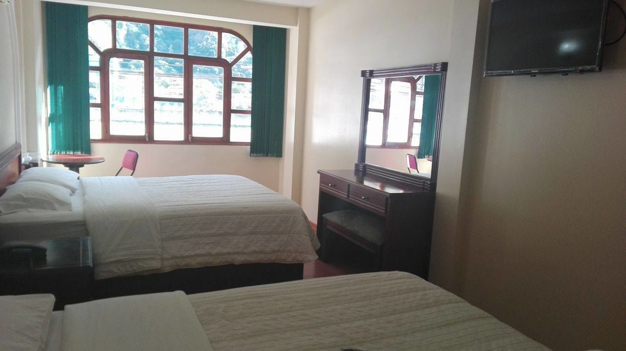 Une chambre avec deux lits, un bureau, une chaise, une commode et un téléviseur fixé au mur.