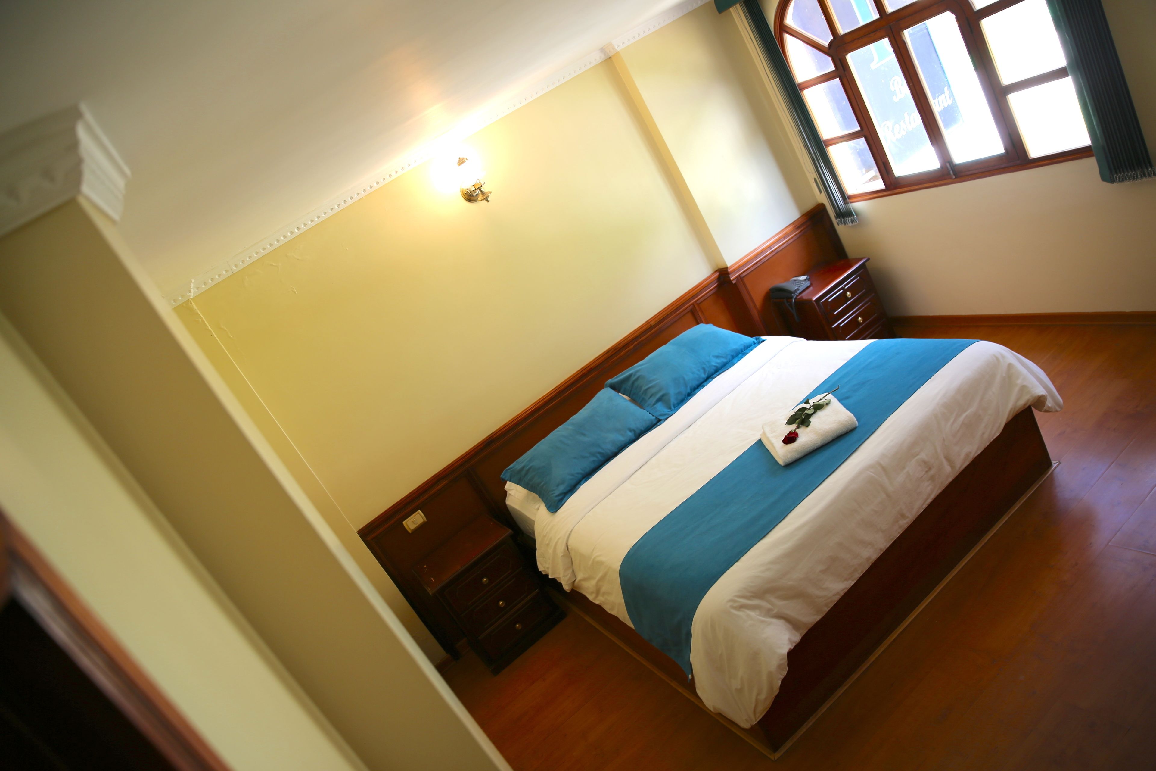 Ein Hotelzimmer mit Bett, Nachttisch, Kommode und einem Fenster mit Vorhängen.