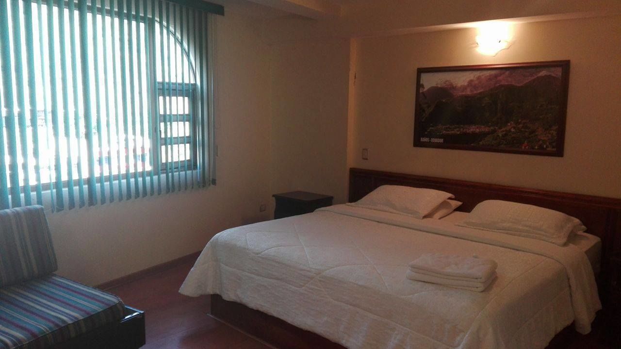 A hotel room with a bed, a chair, a nightstand, and a painting on the wall.