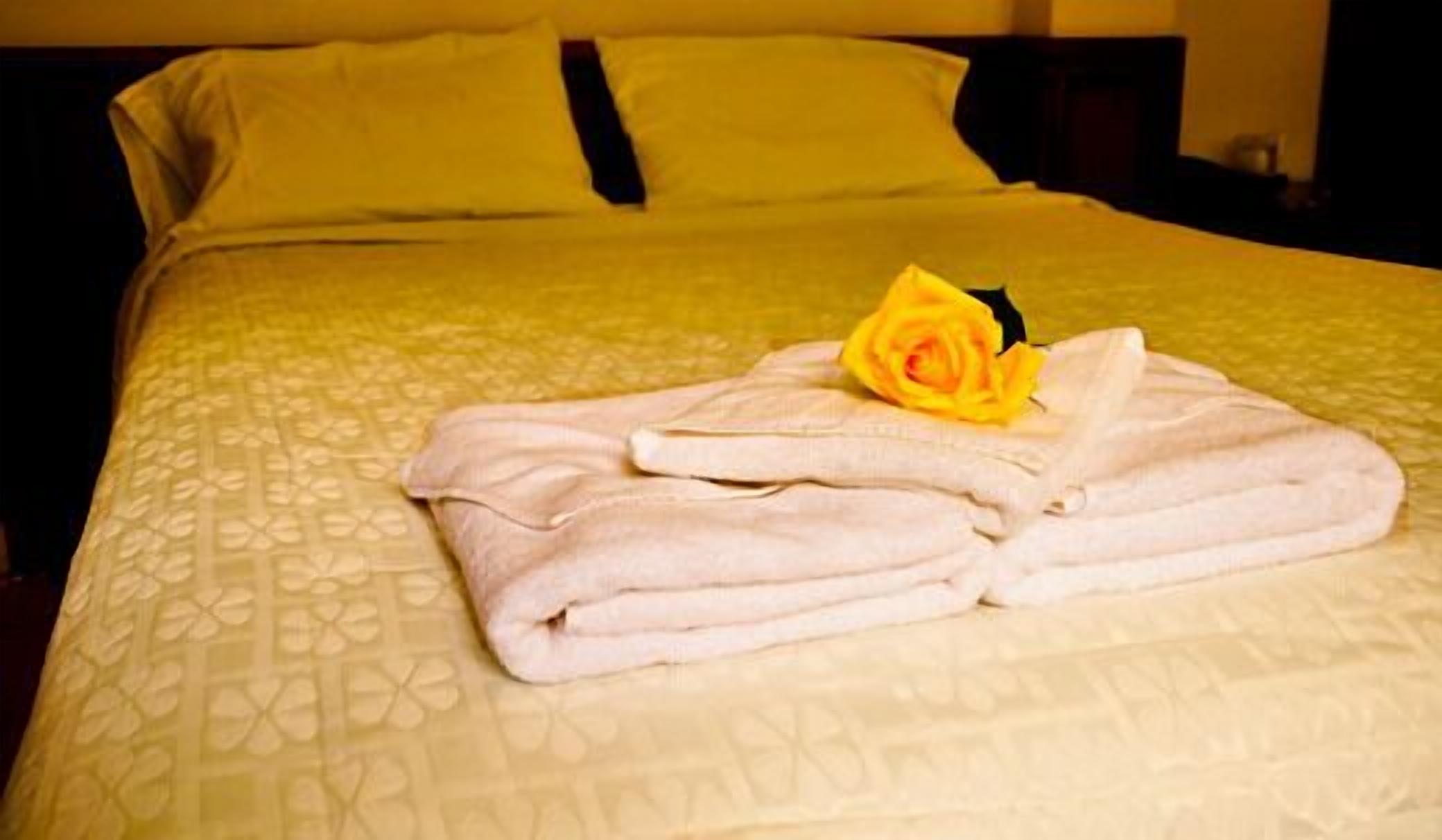 A neatly made bed with a folded towel and a single rose on the bedspread.