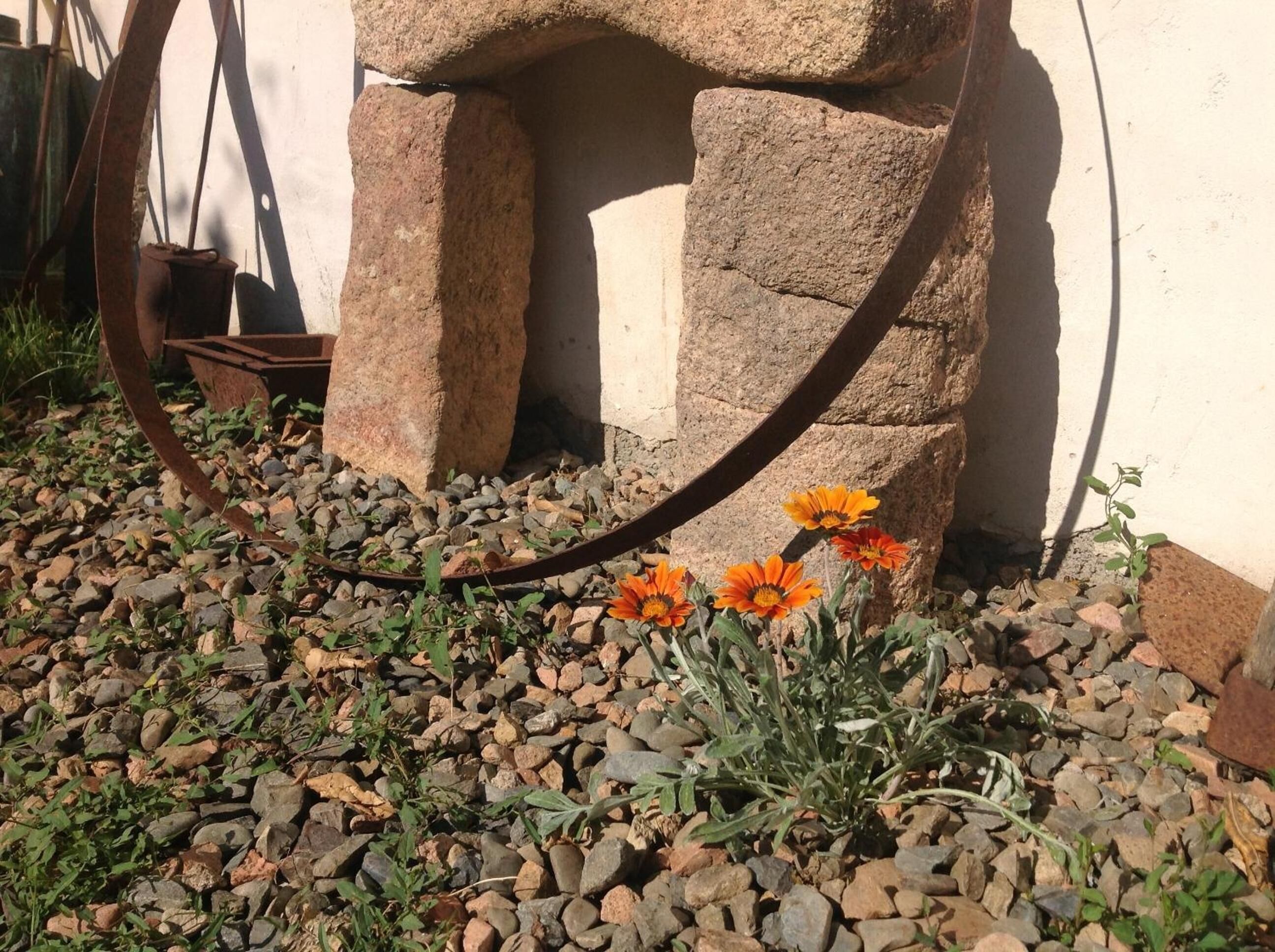 A garden with a stone structure, gravel ground, and orange flowers.