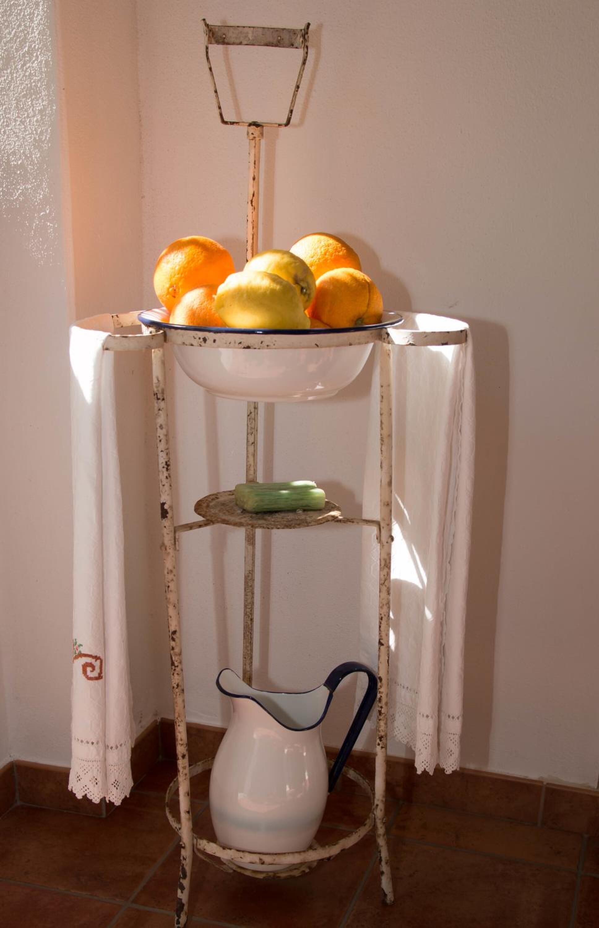 A rustic metal shelf with a white tablecloth, holding oranges and lemons, and a white pitcher.