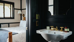 Une chambre d’hôtel avec un lit, un lavabo blanc doté de robinets dorés et un miroir au-dessus du lavabo.