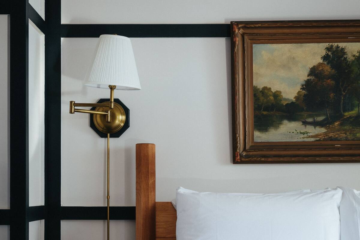 A bedroom with a bed, a nightstand, a lamp, and a painting on the wall.