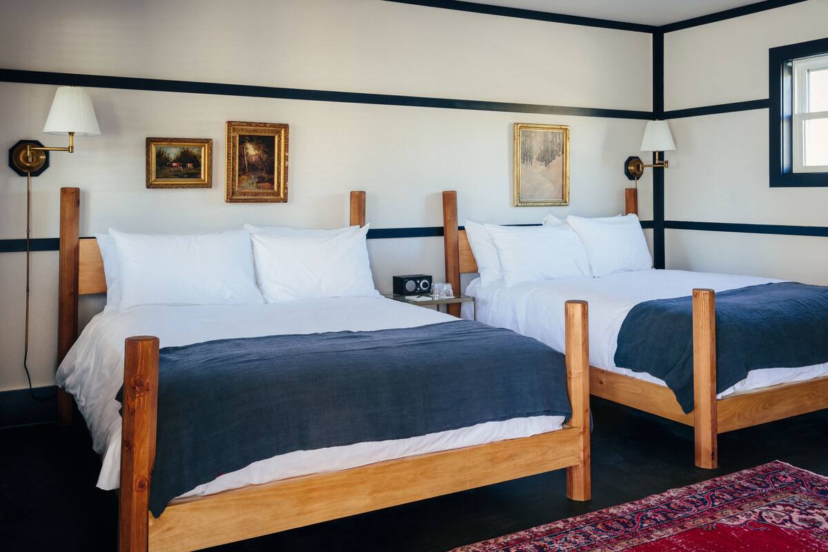 A double room with two wooden beds, white linens, dark blue bedding, and framed artwork on the walls.