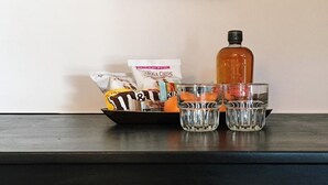 Un meuble en bois avec un tableau accroché au-dessus, un sac de collations, une bouteille et deux verres.
