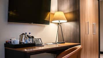 A hotel room with a desk, a chair, a television, a lamp, a minibar, and a wardrobe.