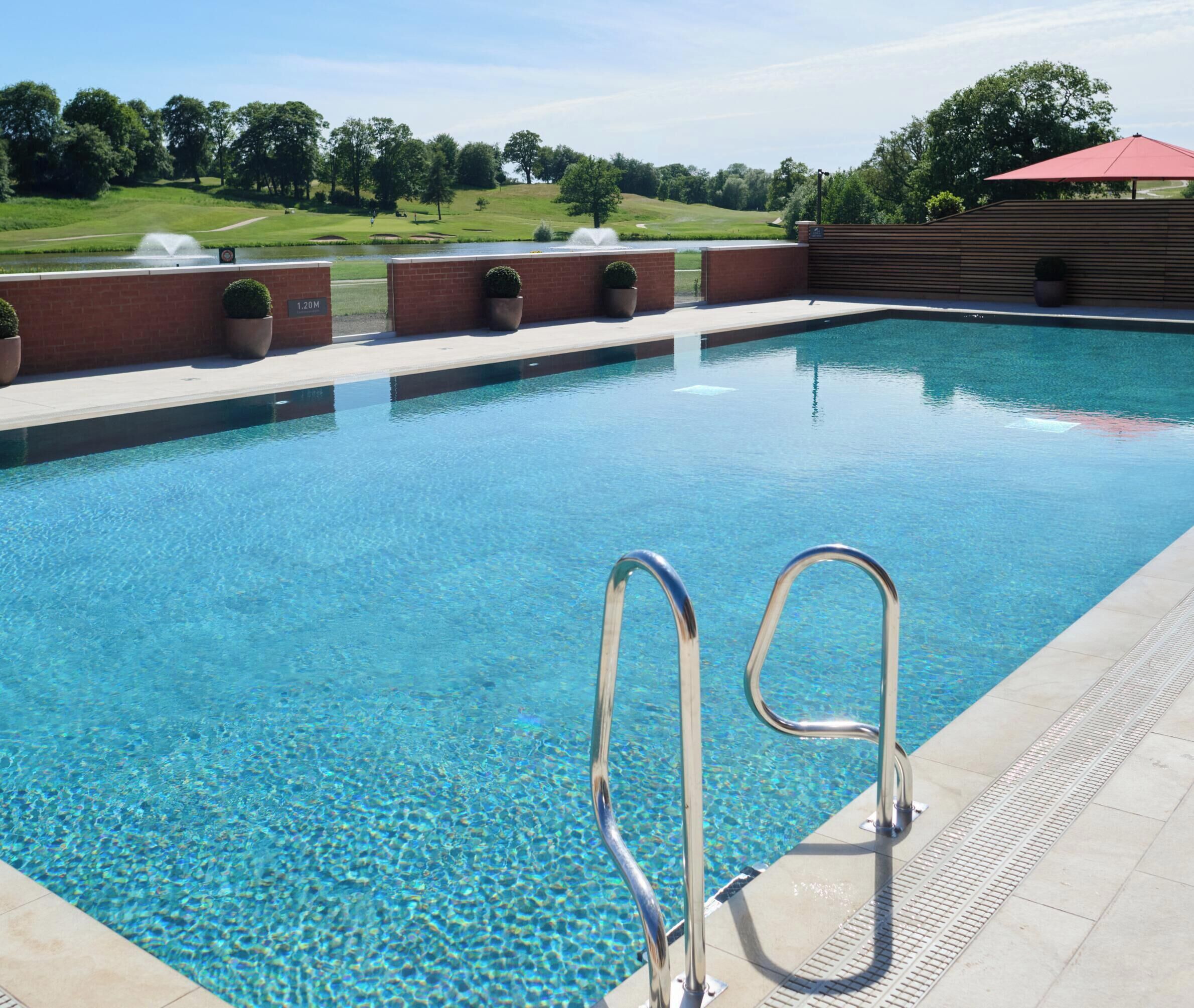 A swimming pool with clear blue water, surrounded by a brick wall and potted plants.