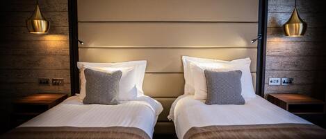 A hotel room with two beds, a wooden wall, and pendant lights.