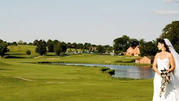 Een golfbaan met een vijver, bomen en een gebouw op de achtergrond.