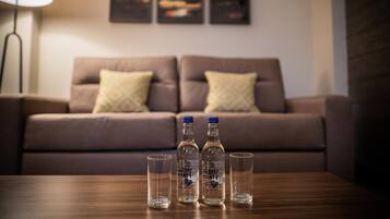 A living room with a brown sofa, two bottles of liquor, and three glasses on a wooden table.