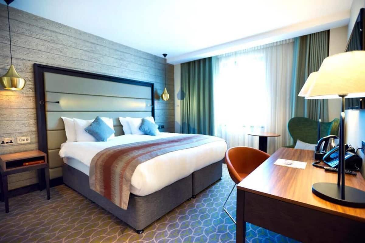 Een hotelkamer met een groot bed, een bureau met telefoon en een stoel.