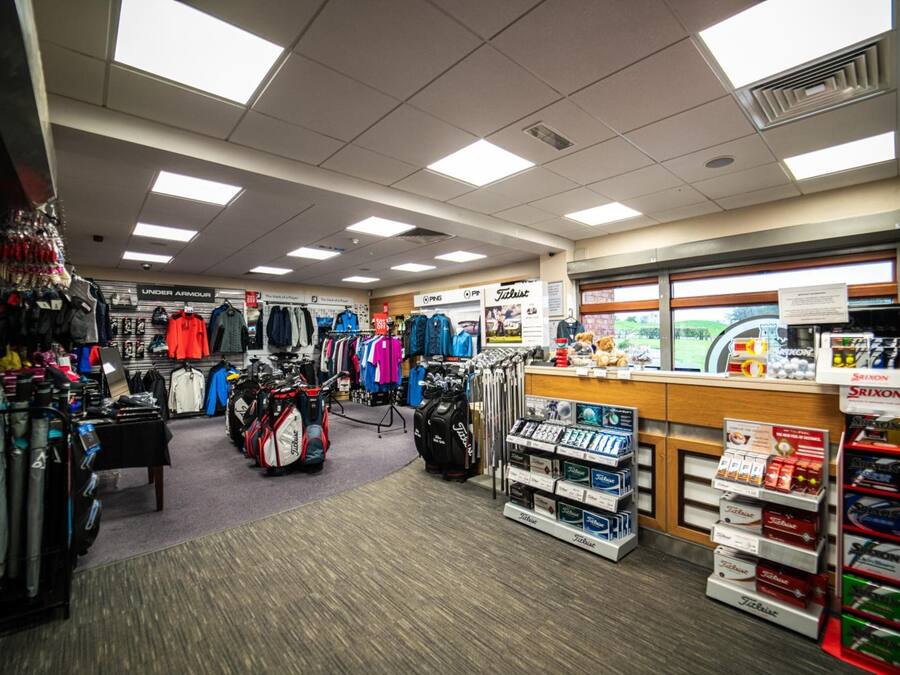 Tienda de artículos de golf con estantes llenos de bolsas, ropa y pelotas.