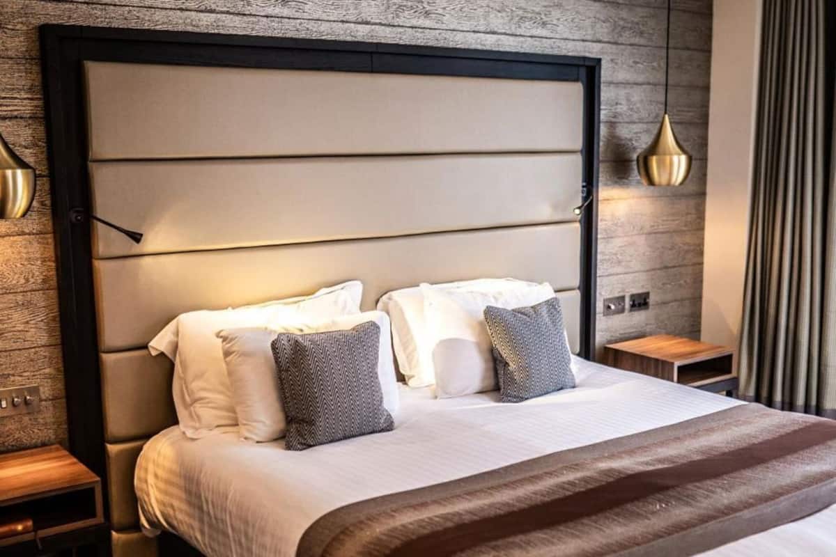 Een moderne hotelkamer met een groot bed, een houten hoofdbord, een nachtkastje en een hangende吊灯.