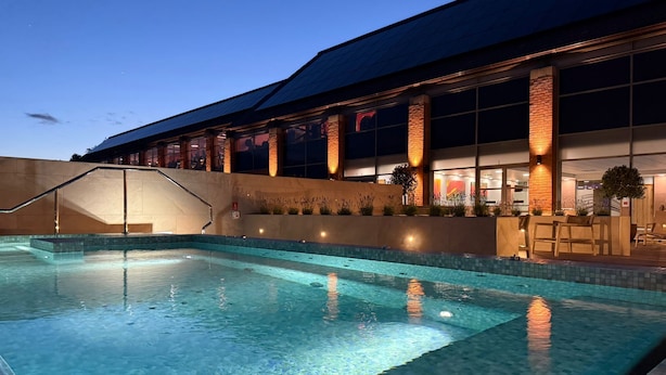 A swimming pool with a tiled edge, a staircase leading to a building, and a building with large windows and columns. - The Warwickshire Hotel and Country Club (Warwick)
