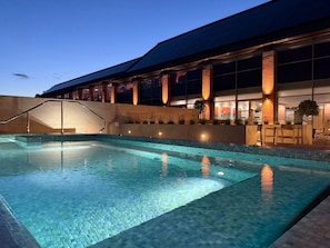 A swimming pool with a tiled edge, a staircase leading to a building, and a building with large windows and columns. - The Warwickshire Hotel and Country Club (Warwick)