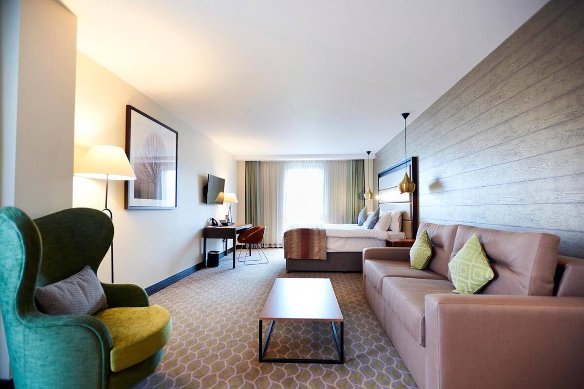 Een hotelkamer met een bank, fauteuil, salontafel, televisie en een bed met hoofdeinde.