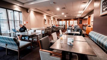 Een restaurantruimte in een hotel met meerdere tafels en banken, een koffiehoek en ingelijste foto's aan de muur.