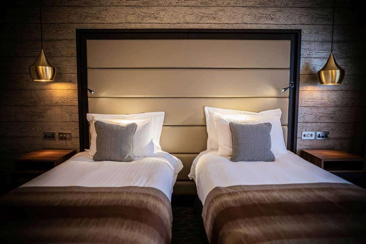 Een tweepersoonskamer met twee bedden, een houten hoofdbord, nachtkastjes en hanglampen.