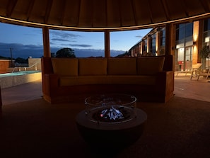 An outdoor seating area with a fire feature, a cushioned bench, and a view of a building in the background. - The Warwickshire Hotel and Country Club (Warwick)