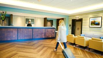 Zona de recepción de un hotel con mostrador, área de espera con sillas y suelo de madera.