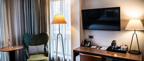 Habitación de hotel con cama, escritorio con silla, televisor, lámpara y ventana con cortinas.