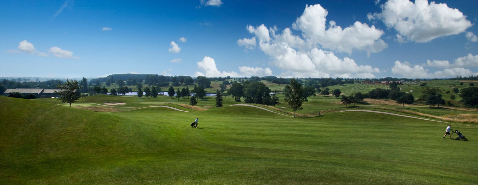 A golf course with well-maintained grass, trees, and a clear sky.