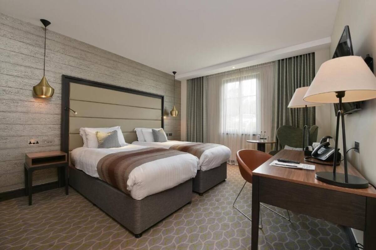 Een hotelkamer met een groot bed, een bureau, een stoel, een lamp en een telefoon.
